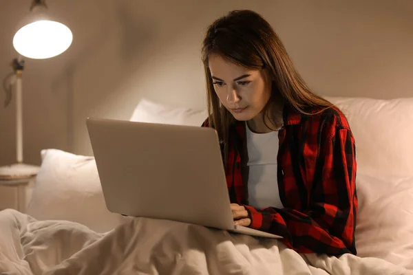 Beautiful woman using laptop in bed at night