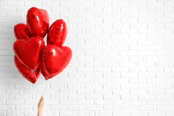 Woman with heart shaped balloons for Valentine\'s Day on white brick background