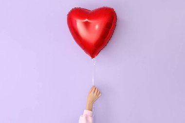 Woman with heart shaped balloon for Valentine's Day on lilac background