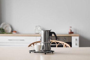 Grid with geyser coffee maker and cup on table in kitchen