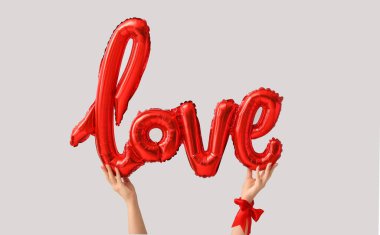 Female hands with balloon in shape of word LOVE on grey background. Valentine's Day celebration