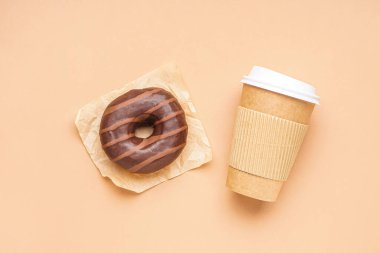 Parchment with delicious chocolate donut and paper cup on beige background