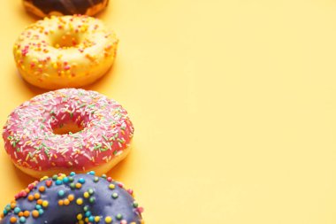 Line made of different delicious donuts on yellow background