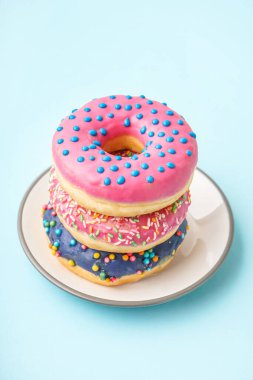 Plate with different delicious donuts on blue background