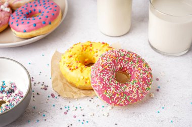 Parchment with delicious donuts and glass of milk on white table