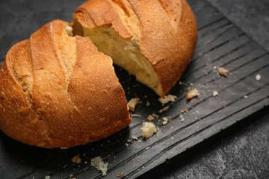 Board with loaf of fresh bread on black background