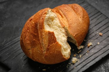 Board with loaf of fresh bread on black background