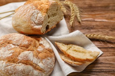 Napkin with loaves of fresh bread and wheat ears on wooden background
