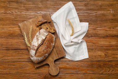 Board with loaf of fresh rye bread and wheat ears on wooden background