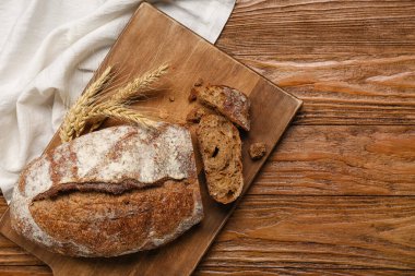 Board with loaf of fresh rye bread and wheat ears on wooden background