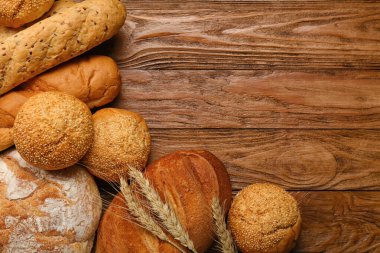 Loaves of different bread and wheat ears on wooden background