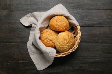 Delicious buns with sesame seeds in wicker basket on black wooden background