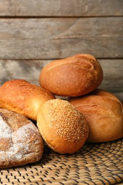 Wicker mat with loaves of different bread on wooden background