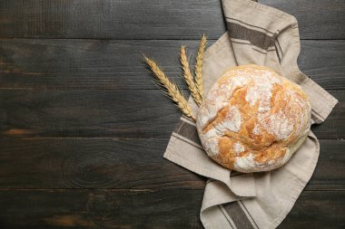 Loaf of fresh bread and wheat ears on black table