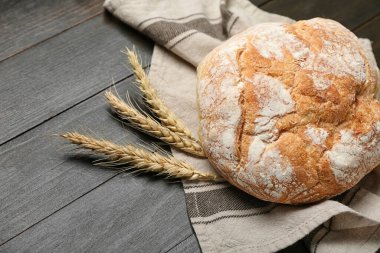 Loaf of fresh bread and wheat ears on black table
