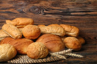 Wicker mat with loaves of different bread and wheat ears on wooden table