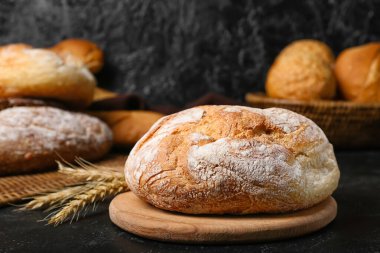 Cutting board with loaf of fresh bread and wheat ears on black table