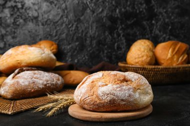 Cutting board with loaf of fresh bread and wheat ears on black table