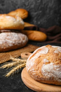 Cutting board with loaf of fresh bread and wheat ears on black table
