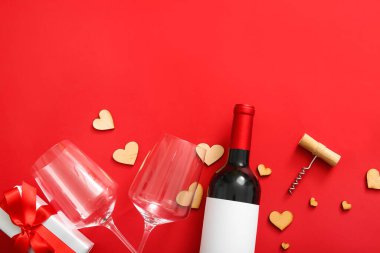Composition with bottle of wine, glasses, corkscrew and decor on red background. Valentines Day celebration