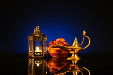 Aladdin lamp of wishes, dates and Muslim lantern for Ramadan on table against dark blue background