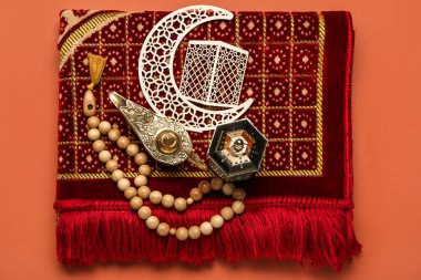 Mat with Aladdin lamp, Muslim lantern, crescent and prayer beads for Ramadan on red background