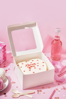 Opened box with tasty bento cake, bottle and confetti on pink table. Valentine's Day celebration