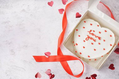 Box with heart-shaped bento cake and ribbon on white background. Valentine's Day celebration