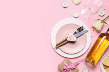 Table setting with bottle of wine, cookie, rose flower, glasses and gift on pink background. Valentine's Day celebration