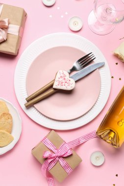 Table setting with bottle of wine, cookie, glasses and gifts on pink background. Valentine's Day celebration