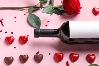 Composition with bottle of wine, rose flower and chocolate candies on pink background. Valentine's Day celebration