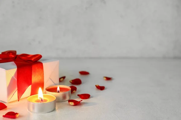 Burning candles, gift box and rose petals on light background. Valentine\'s Day celebration