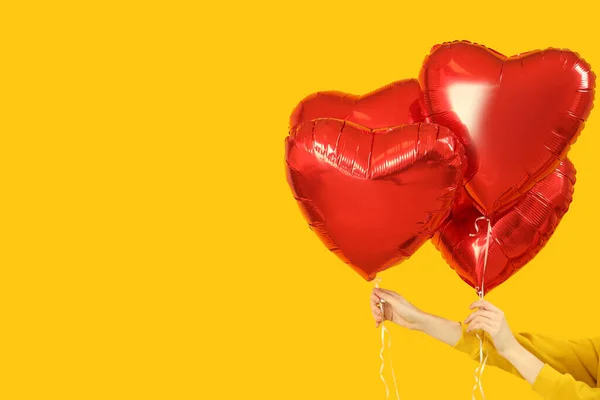 Woman with heart-shaped balloons for Valentine's Day on yellow background