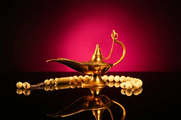 Aladdin lamp of wishes and prayer beads for Ramadan on table against dark red background