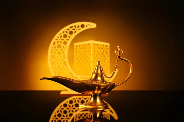 Aladdin lamp of wishes and decorative crescent for Ramadan on table against dark yellow background