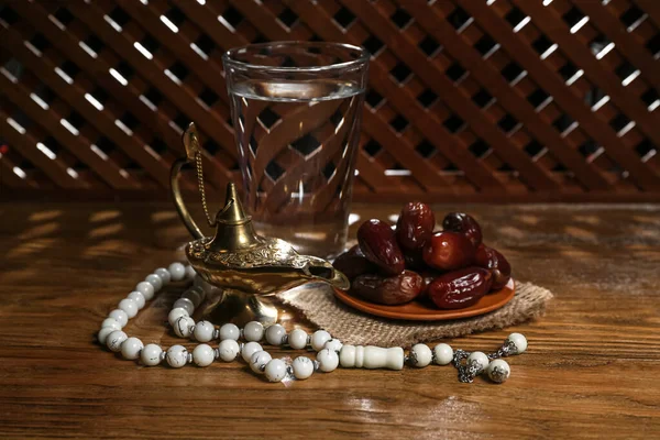 Aladdin lamp of wishes, prayer beads, glass and dates for Ramadan on wooden table