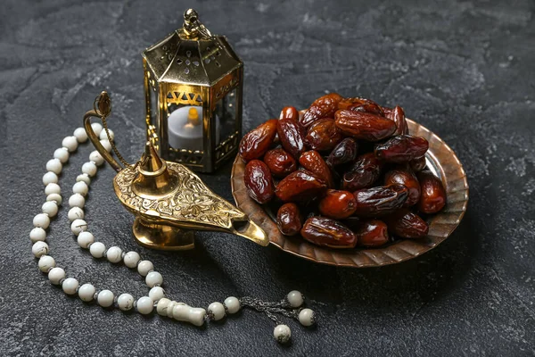 Aladdin lamp of wishes, dates, Muslim lantern and prayer beads for Ramadan on dark background