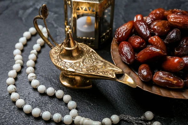 Aladdin lamp of wishes, dates, Muslim lantern and prayer beads for Ramadan on dark background, closeup