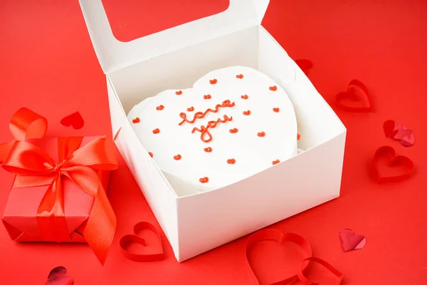Opened box with heart-shaped bento cake and gift on red background. Valentine\'s Day celebration