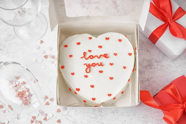 Box with heart-shaped bento cake, glasses and gifts on white background. Valentine\'s Day celebration