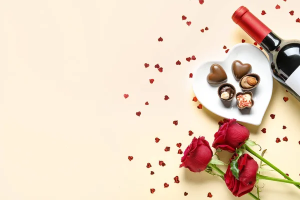 Bottle of wine, chocolate candies and rose flowers on beige background. Valentine\'s Day celebration