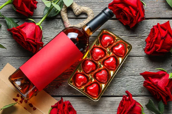 Bottle of wine, box with candies and rose flowers on grey wooden background. Valentine\'s Day celebration