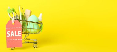 Shopping cart with makeup products and sale tag on yellow background with space for text