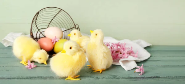 Cute chickens, overturned basket with Easter eggs and flowers on wooden table