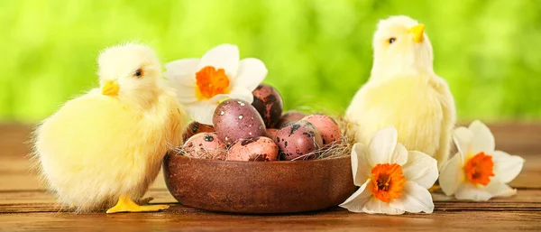 Cute chickens, Easter eggs and flowers on table outdoors