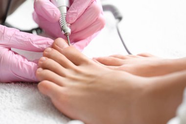 Young woman getting pedicure with milling cutter in beauty salon, closeup
