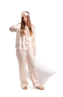 Upset young woman with sleeping mask and pillow on white background