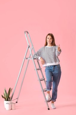 Young woman with ladder showing thumb-up on pink background