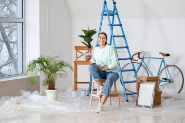 Young woman with paint can sitting on stepladder at home