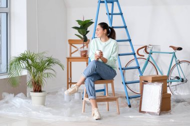 Young woman with paint can sitting on stepladder at home